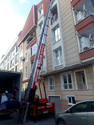 Dar sokakta kamyondan apartman balkonuna uzanan asansör kolu