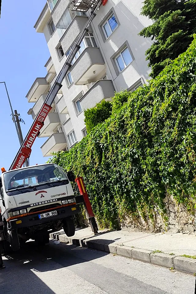 Bir sokakta kurulmuş, apartman cephesine uzanan kırmızı Doğuş Asansör kolu